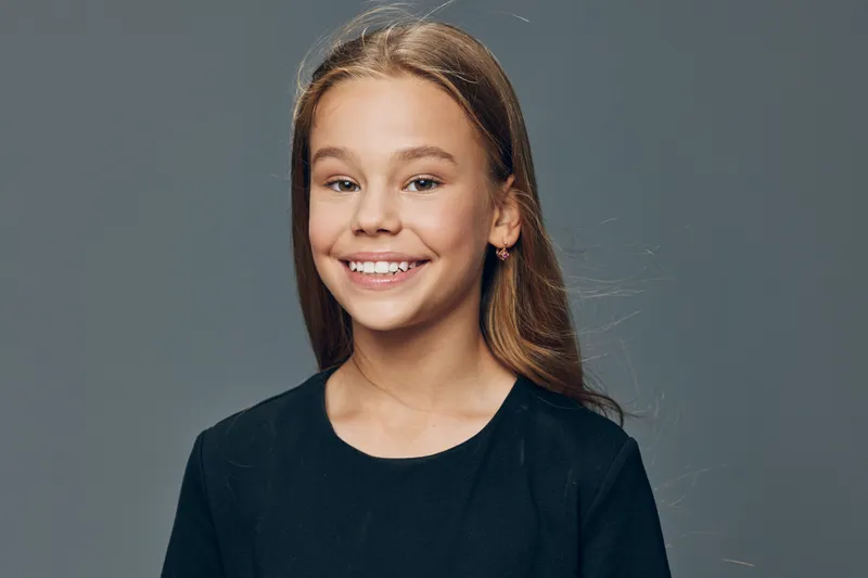 Girl portrait smiling with long hair and casual black t shirt against plain gray background. Happy child with natural expression and youthful appearance looking at camera.