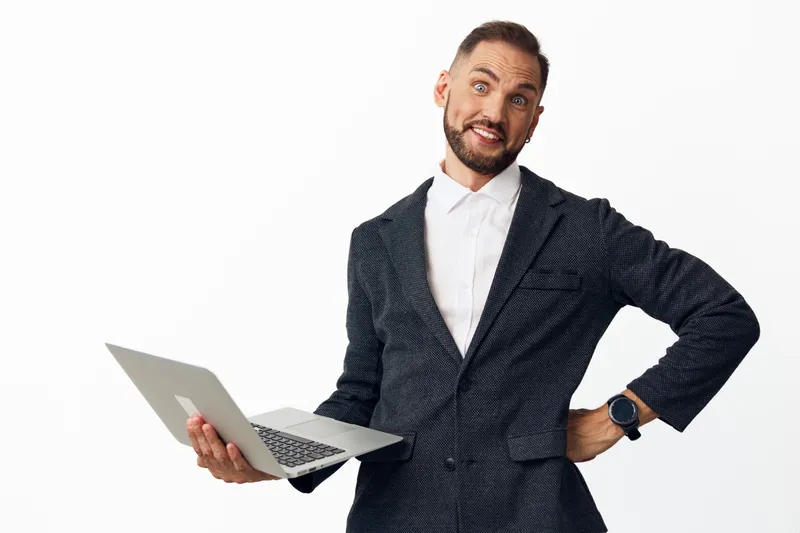Professional man in business attire holds a laptop with confident smile, showcasing leadership and energy against a clean colored background, embodying focus and productivity.
