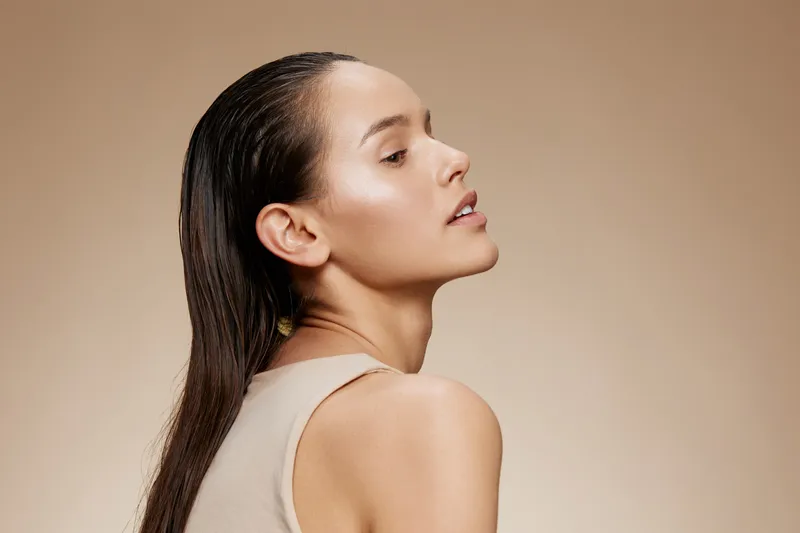 Young woman with wet hair posing against a beige background, conveying serenity and confidence, ideal for beauty and skincare concepts