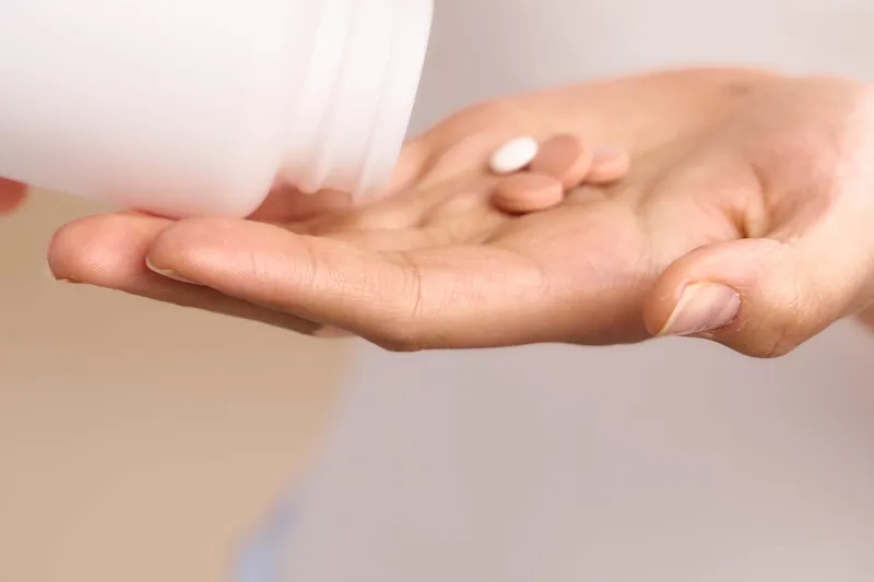 asian woman pours pills from a bottle into her palm, preparing a dose in a calm home setting, conveying health awareness and mindful medication use. warm light highlights careful routine.