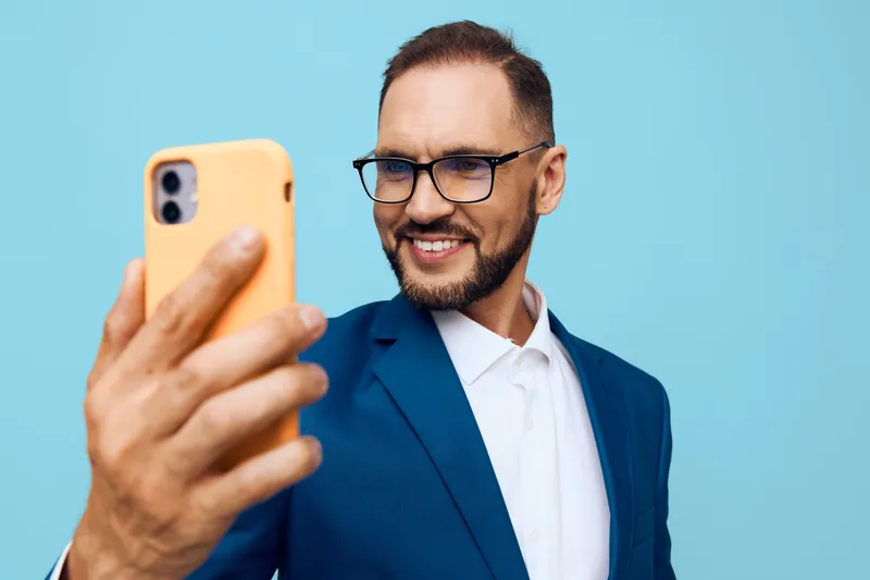 A professional man in a blue suit takes a confident selfie against a solid colored background, conveying focus, ambition, and a positive business mood.