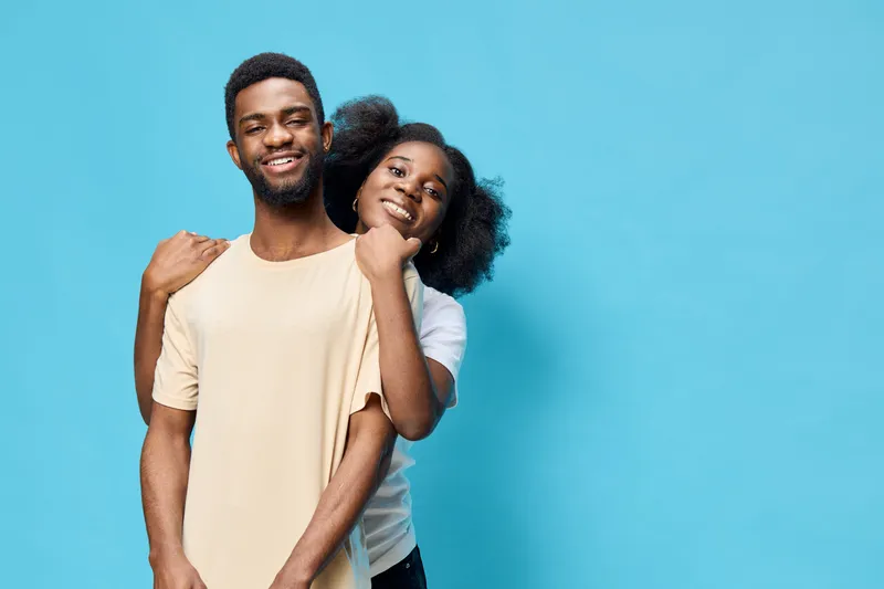 Happy young couple standing together against a bright blue background, expressing love and joy, showcasing their casual summer outfits and natural smiles