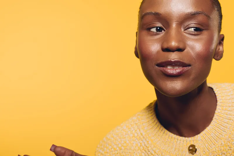 Close-up of a smiling African woman with dark skin wearing a yellow sweater on yellow background. Concept of beauty, confidence, and diversity in portrait photography.