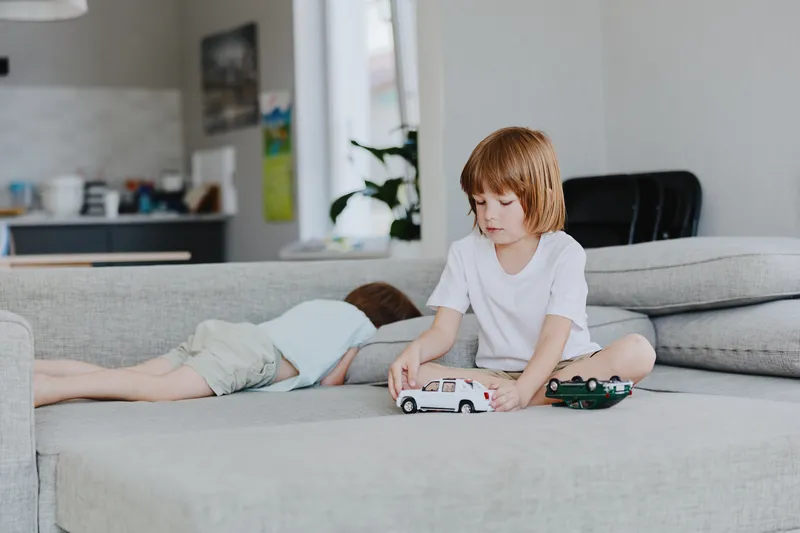Young boy playing with toy cars, indoors, cozy living room setting, focused expression, soft colors and natural light make the scene feel inviting.