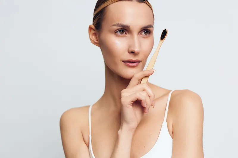 Young woman with clear skin holding a bamboo toothbrush near her face, natural beauty concept, minimal makeup, clean background, healthy lifestyle focus