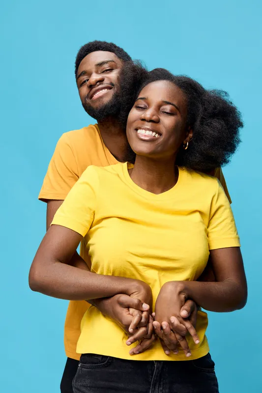 Happy couple embracing against a vibrant blue background, showcasing joy and affection, wearing bright yellow and orange shirts, representing love and connection