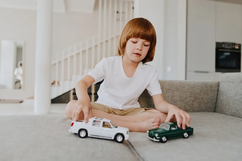 Young boy playing with toy cars in a bright and modern living room, showcasing creativity and childhood joy. Perfect for themes of childhood and leisure activities.