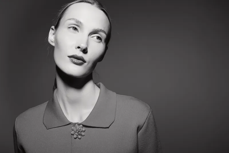Portrait of a pale skinned Caucasian woman with slicked back hair wearing a vintage sweater, looking thoughtfully to the side.