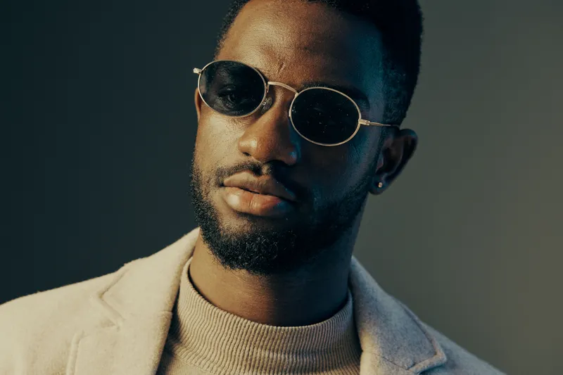 Stylish African man with sunglasses in a modern outfit, exuding confidence and sophistication against a minimalistic background, perfect for fashion and lifestyle themes