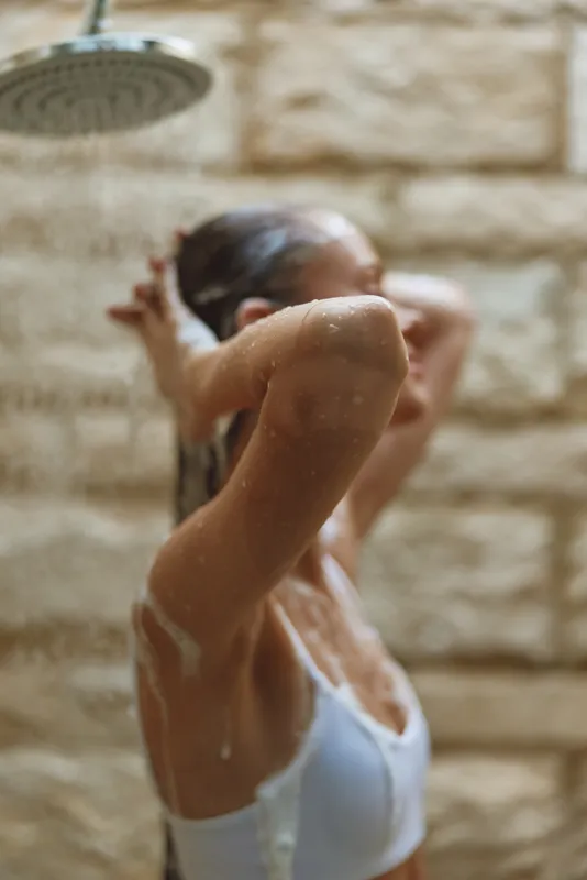 Woman taking shower indoors with water running, cleansing and relaxing under a stone wall. Natural skin care, fresh morning routine, wellness and self-care concept.