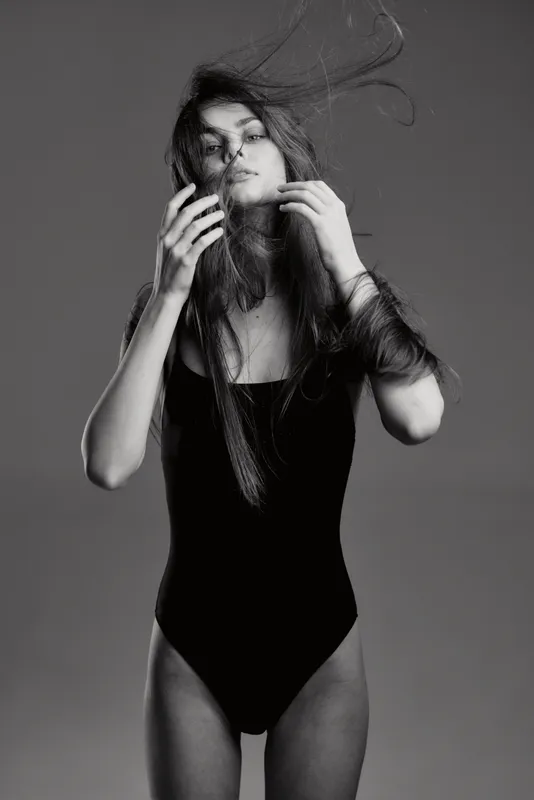 Black and white artistic portrait of a young woman in a black leotard with flowing hair and expressive pose