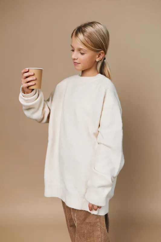 Authentic scene of a young girl in a cozy sweater holding a cup, capturing a simple school lifestyle moment with calm focus and quiet everyday charm.