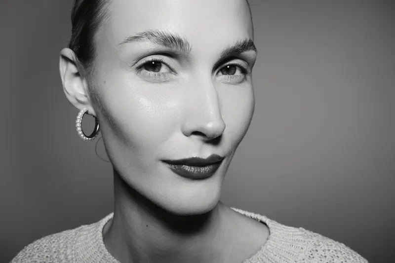 Close-up portrait of a fair skinned Caucasian woman with short hair wearing hoop earrings and a sweater. Studio lighting highlights her confident expression and clear skin.