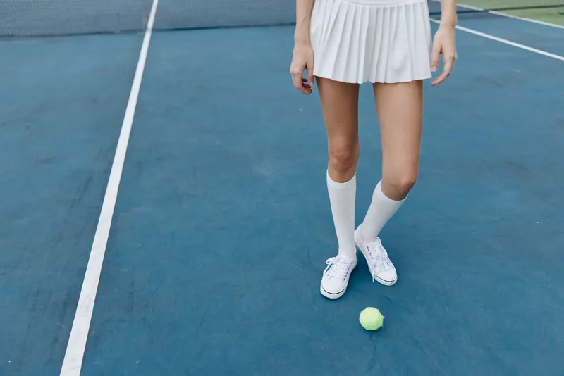 Female tennis player in a sporty white outfit standing on a blue court, showcasing athleticism, determination, and focus, with a tennis ball at her feet