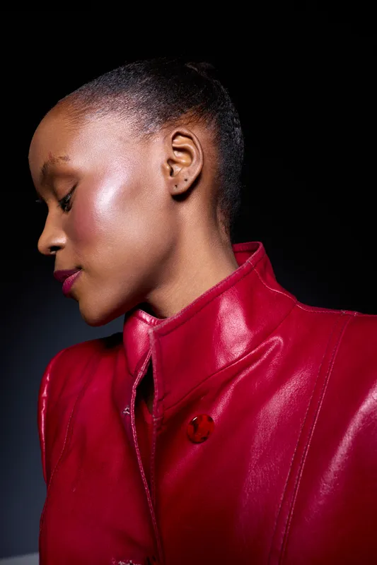 Portrait of a dark skinned African woman with eyes closed wearing a red leather jacket. Studio shot with dramatic lighting highlights smooth skin and elegant profile. Concept of fashion and beauty.