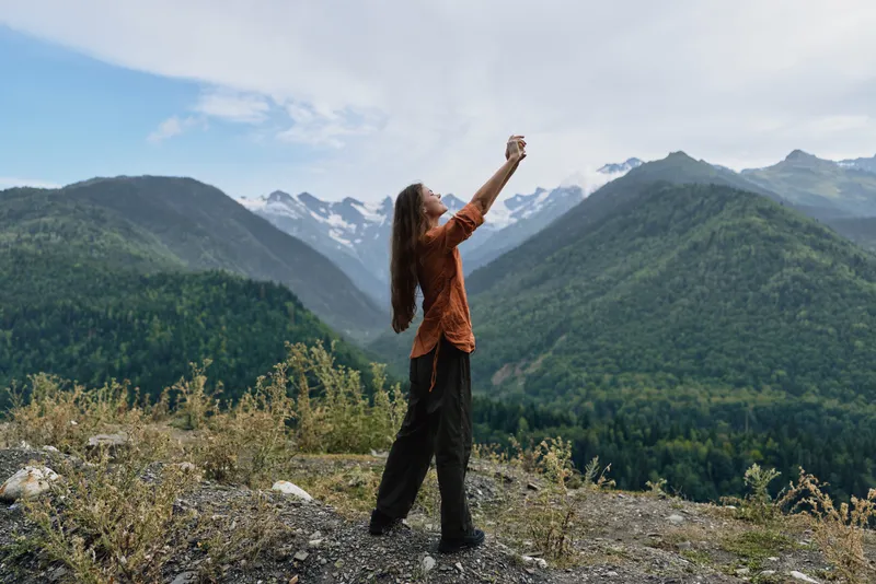 woman mountains smartphone nature authenticity inclusivity hiking landscape, solo traveler photographing valley and snow peaks on ridge during golden hour