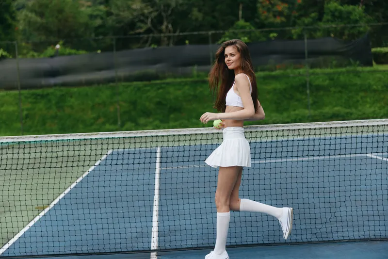 Young woman in sporty white outfit smiling on a tennis court, enjoying a sunny day and showcasing an active lifestyle and athletic spirit