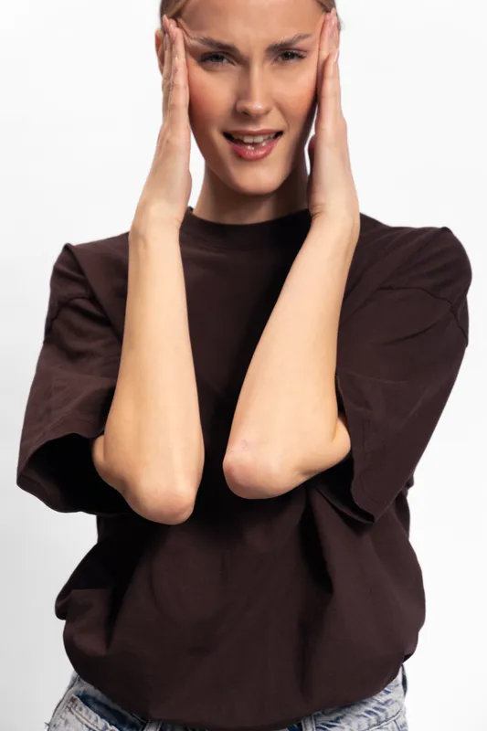 Young woman in brown shirt holds head with hands and shows pain or discomfort, isolated on white background. Concept for stress, headache, and emotional tension.