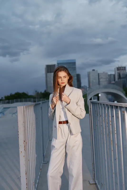 Confident business woman in a tailored outfit, showcasing professionalism against a modern urban backdrop with a dramatic sky.