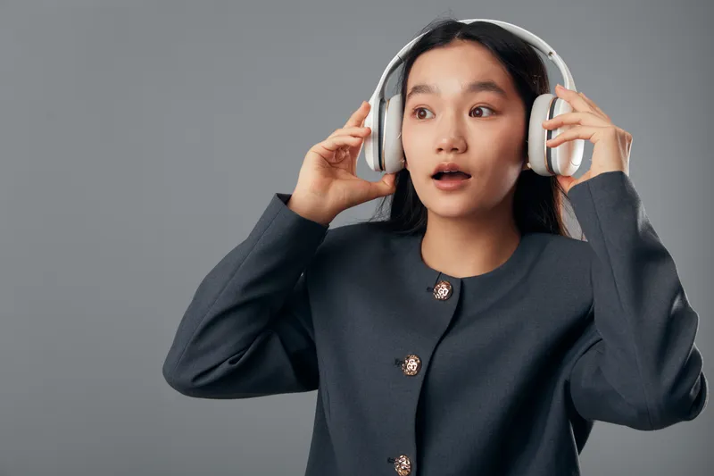 Young woman wearing headphones with surprised expression listening to music or podcast, casual clothing and dark background with copy space for technology or lifestyle concept.