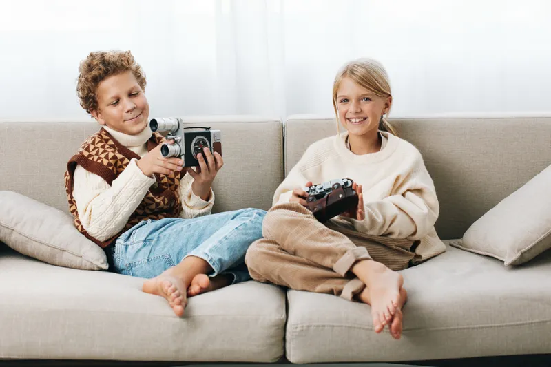 Authentic moment of youth at play, children explore photography and gaming on a comfy sofa, a simple school inspired lifestyle scene celebrating curiosity.