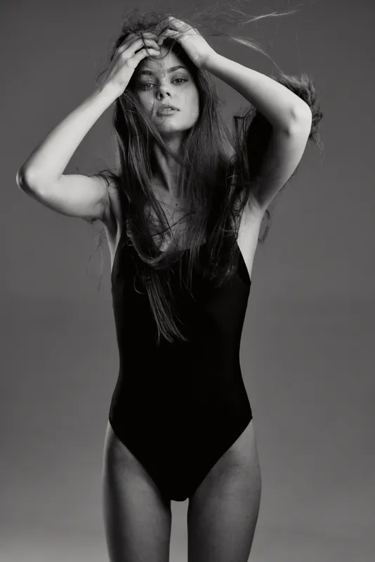 Black and white portrait of a woman in a black bodysuit with messy hair and intense expression, artistic mood.