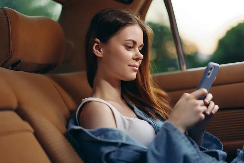 Young woman enjoying a moment of relaxation in a car, casually dressed in denim, looking at her phone, conveying a sense of tranquility and comfort.