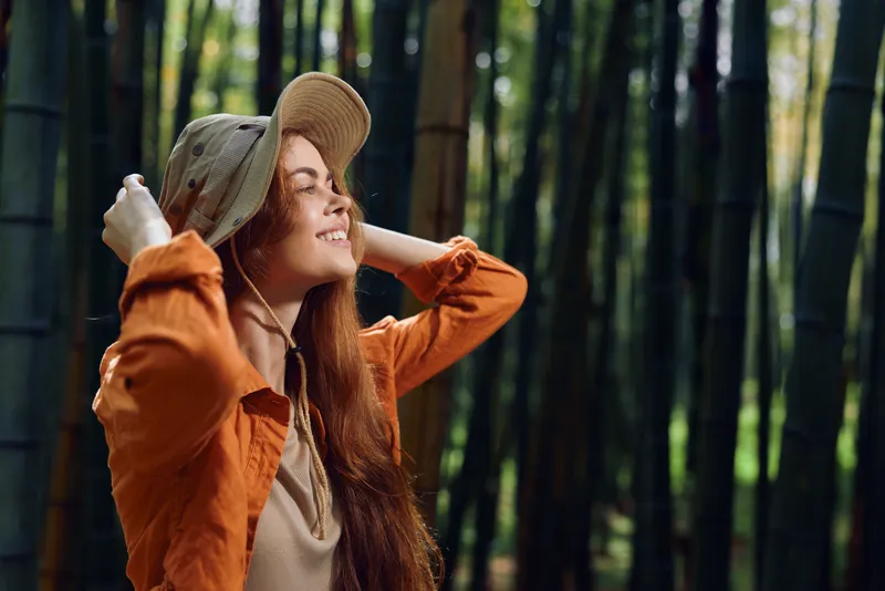 woman smile hat bamboo forest nature redhead happiness young female portrait standing among tall bamboo trees, enjoying sunlight and fresh air in casual clothing with relaxed joyful expression