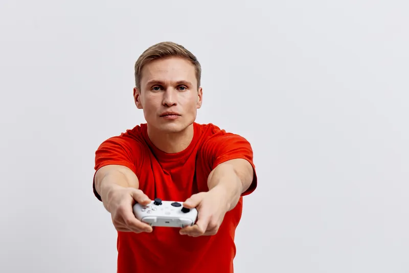 young caucasian man hold video game controller wear red t-shirt focused look camera isolated on plain background entertainment concept