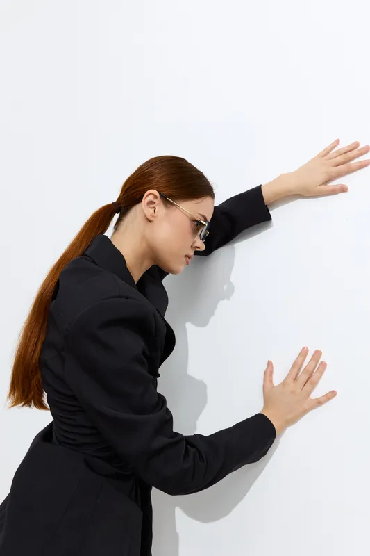 fashion woman with long red hair wearing black blazer and glasses posing against white background in modern minimalistic style