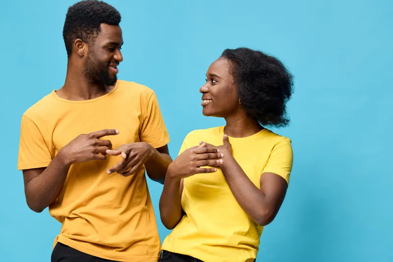 Young African American couple wearing yellow and orange shirts against a blue background, expressing joy and connection in a vibrant summer atmosphere