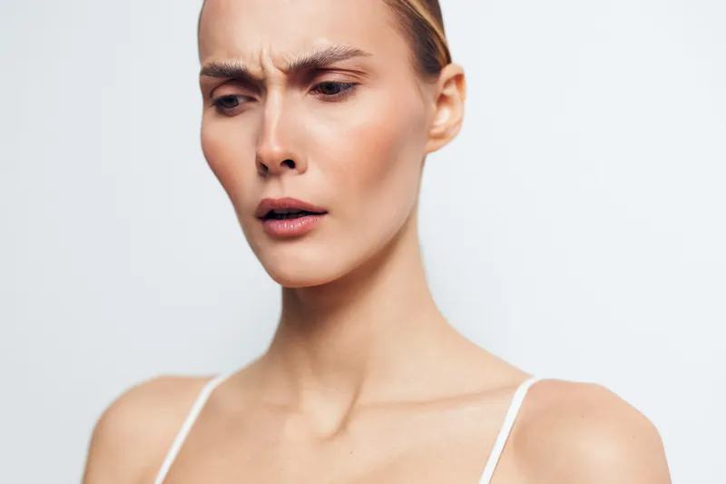 Close-up portrait of a thoughtful woman, tense expression, soft studio lighting, clean background, natural makeup, subtle shadows, conveying concentration