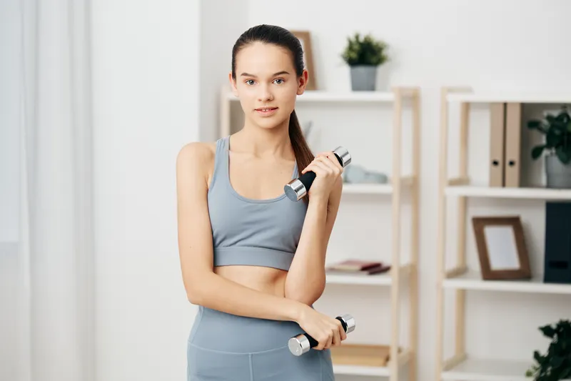 Fitness, woman, workout, dumbbells, training, exercise, health, indoors. A fit woman in gymwear lifts dumbbells in a bright, modern room with shelves and plants, showcasing home fitness, strength