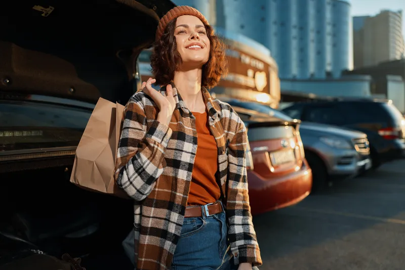 woman shopping by car trunk in urban parking, smile and casual outfit during golden hour, candid lifestyle shot with authenticity, mindful living vibe and emotional storytelling glow