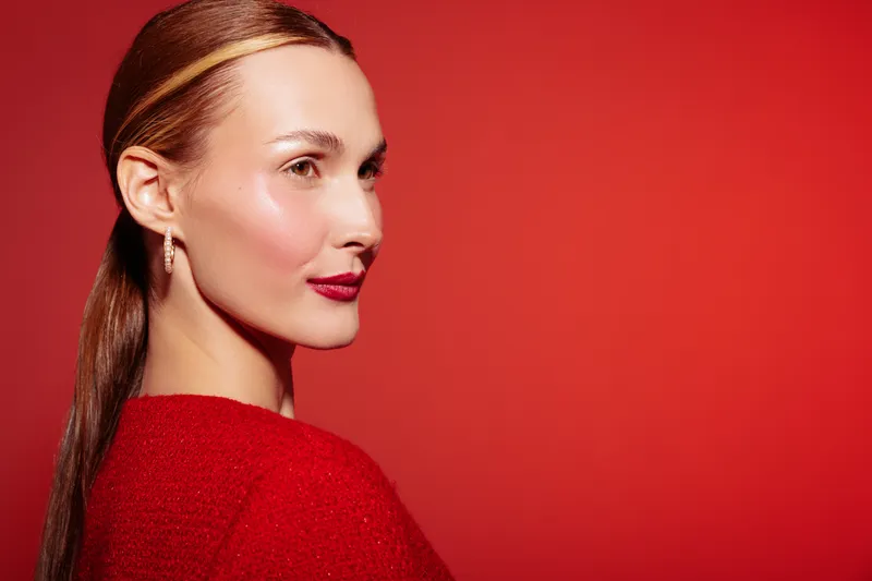 Portrait of confident woman with red lipstick and sleek hair wearing red sweater against red background. Concept of beauty, fashion, elegance, and modern style in studio lighting.