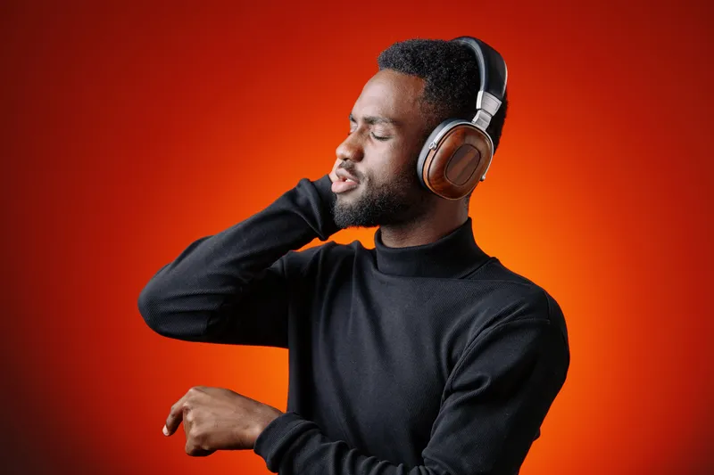 Young African man enjoying music with headphones, wearing a stylish black turtleneck, set against a vibrant orange background, evoking joy and relaxation