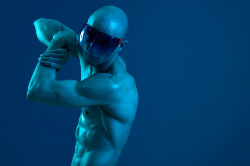 Athletic man stretching his muscles under a blue light, showcasing strength and determination. A striking black and white contrast enhances the dynamic movement.
