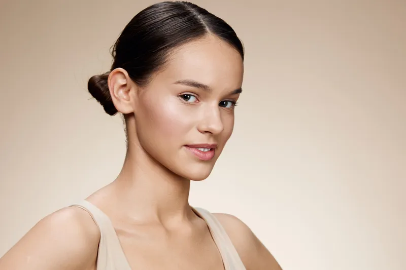 Beautiful young model showcasing natural beauty with soft lighting and minimal makeup, emphasizing skin texture and confidence in a neutral toned backdrop