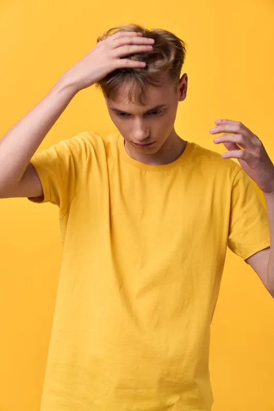 Male model in a yellow t shirt touches his head with a thoughtful look against a bright yellow background, casual studio shot conveying confusion, introspection, mood, fashion, emotion and body