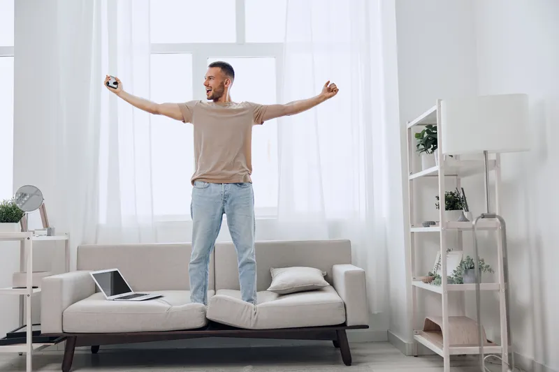 Energized man celebrating his success at home, bright and modern living room. The atmosphere is filled with joy and optimism, making it a perfect image for motivation.