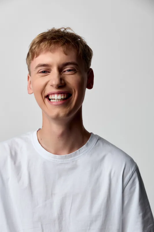 Smiling young man in a white t shirt radiates happiness and approachability, ideal for lifestyle, wellness, and positive branding campaigns.
