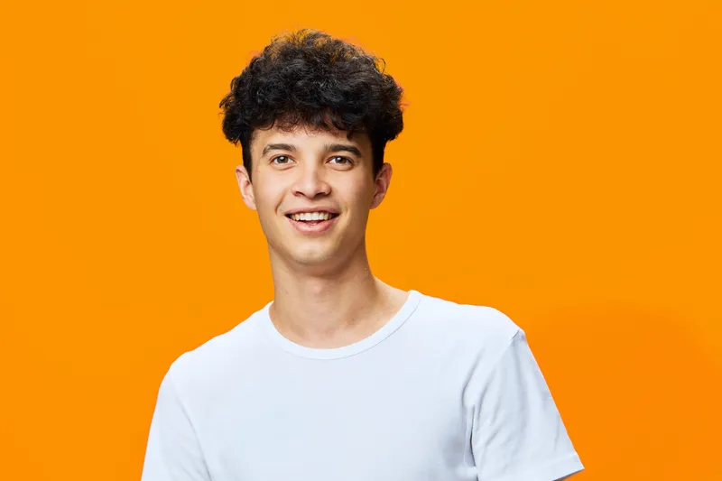 smiling man with curly hair wearing white t-shirt posing joyfully against vibrant orange background expressing happiness and youthfulness