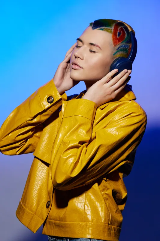 woman with colorful artistic hair wearing yellow jacket enjoys music, closed eyes, serene expression, vibrant background, creative fashion portrait