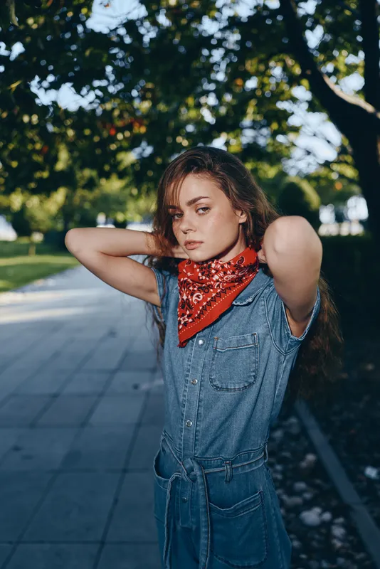 lifestyle woman in modern boho-western denim street style wearing red bandana outdoors with natural sunlight, film color effect, casual and confident expression