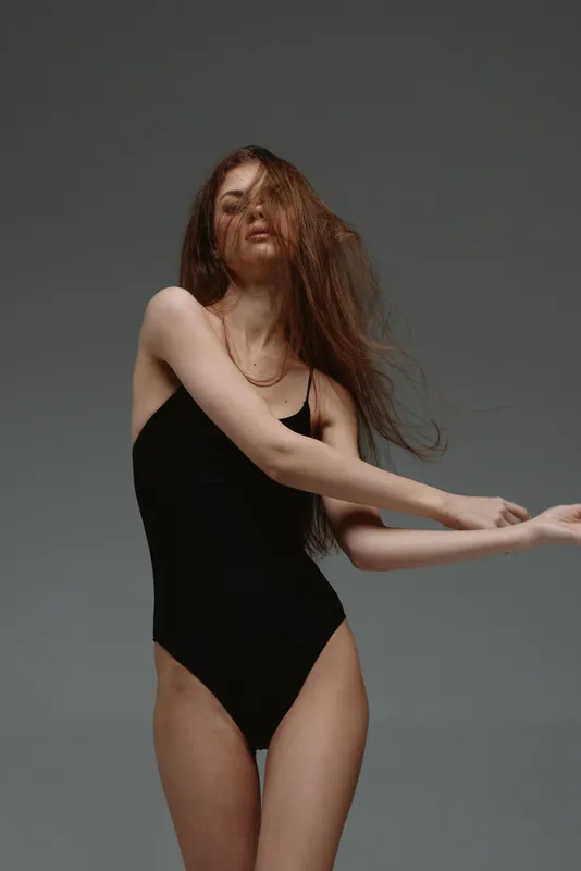 Young woman wearing black bodysuit posing with flowing hair, studio portrait with neutral background, fashion, beauty, confidence