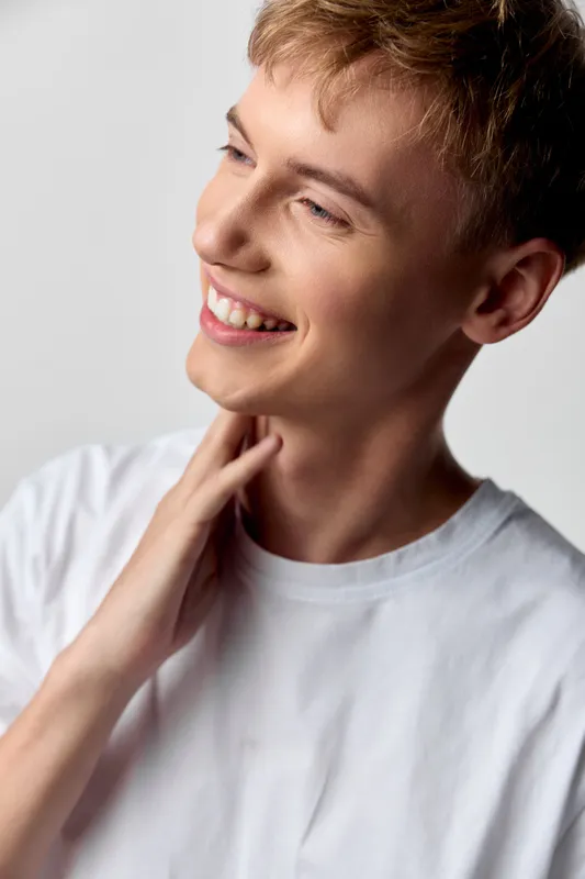 Smiling man in a whiteshirt touches his neck, presenting a lighthearted moment of casual joy and confidence, ideal for lifestyle, wellness and positive communication campaigns