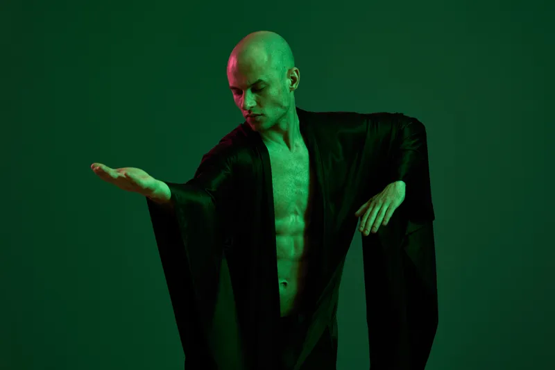 Stylish man in green lighting with a focused expression, showcasing dynamic movement in his elegant attire. A captivating portrayal of grace and poise.