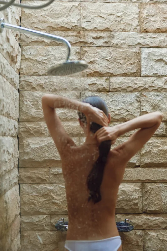 woman showering outdoors under rainfall in a natural stone wall shower space, relaxed mood, wet hair, summer wellness moment