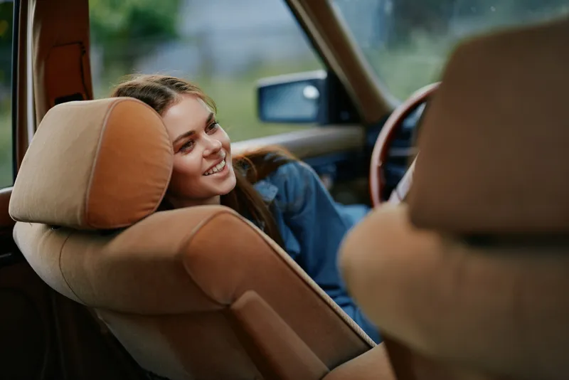 A happy young woman enjoying a peaceful moment in a vintage car, highlighting a relaxed and joyful mood, embracing nostalgia and comfort with natural lighting.