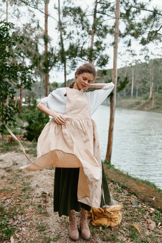 Young woman in a flowing beige dress and green skirt by a serene lake, embodying a sense of tranquility and nature Style reflects bohemian aesthetics and seasonal fashion